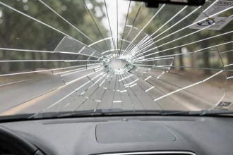 Pare-brise fissuré vu de l'intérieur d'une voiture avec réseau de fissures en toile d'araignée sur le verre feuilleté