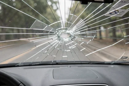 Pare-brise fissuré vu de l'intérieur d'une voiture avec réseau de fissures en toile d'araignée sur le verre feuilleté